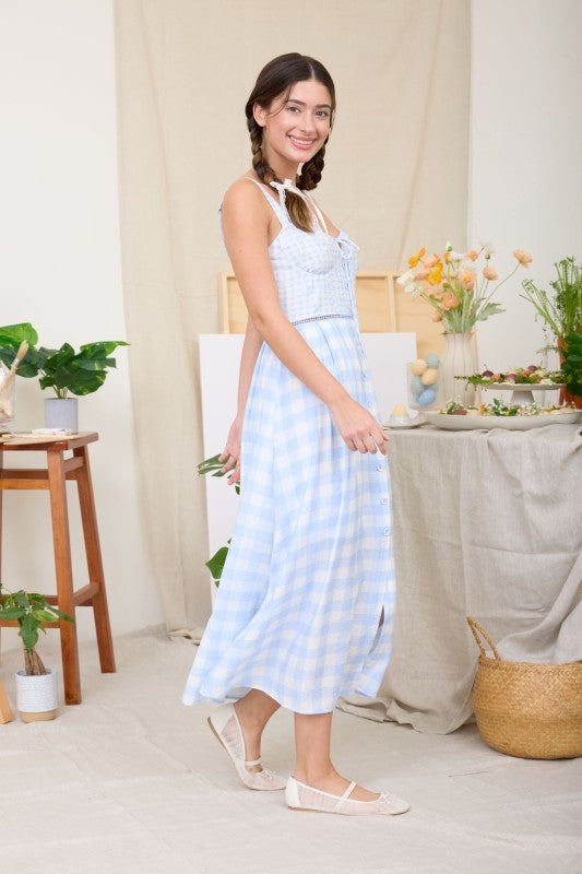 Woman wearing a white top and blue checkered skirt in a home setting with plants and furniture.